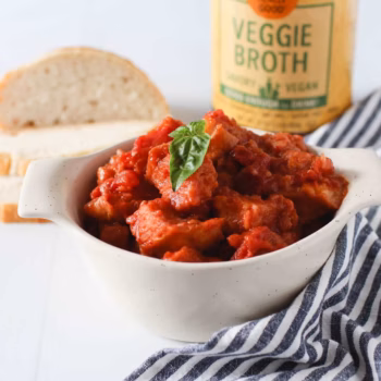 a white ramekin filled with diced bread in a red sauce, topped with a single basil leaf, in front of jar of Zoup Veggie Broth