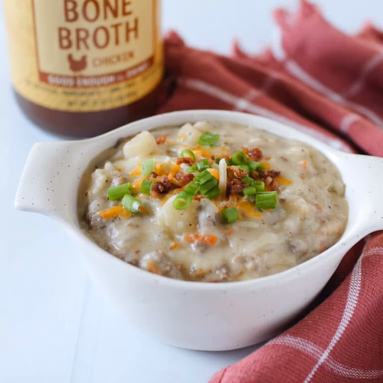 Creamy, chunky soup with ground beef and potatoes topped with shredded cheese, chives and bacon bits, in front of a jar of Zoup Chicken Bone Broth
