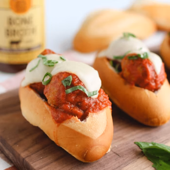 Toasted hoagie rolls filled with meatballs in marinara sauce, melted mozzarella, and fresh basil, with a jar of Zoup Beef Bone Broth blurred in the background.