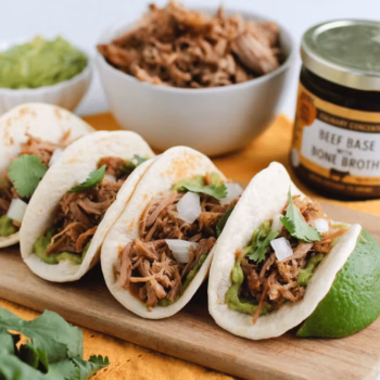 Three corn tortillas filled with carnitas, topped with chopped white onion, fresh cilantro, and diced green peppers.