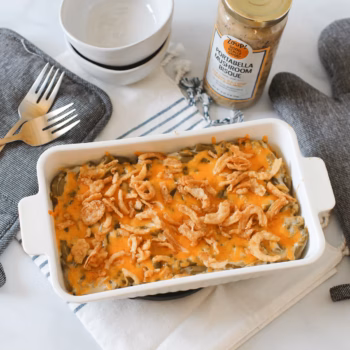 Green bean casserole topped with crispy onions and cheese, with Zoup Portabella Mushroom Bisque and kitchen items in the background.