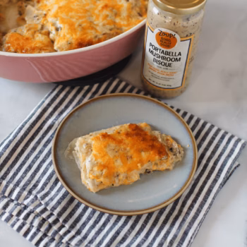 Creamy scalloped potatoes baked with golden cheese topping, served on a blue plate, next to a jar of Zoup Portabella Mushroom Bisque and a pink casserole dish