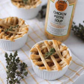 A jar of zoup chicken potpie soup next to several ramekins filled with easy chicken potpie, and topped with a crosshatch pie crust.