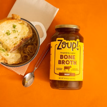 Overhead view of a bowl of brothy chicken soup beside a jar of Zoup chicken bone broth